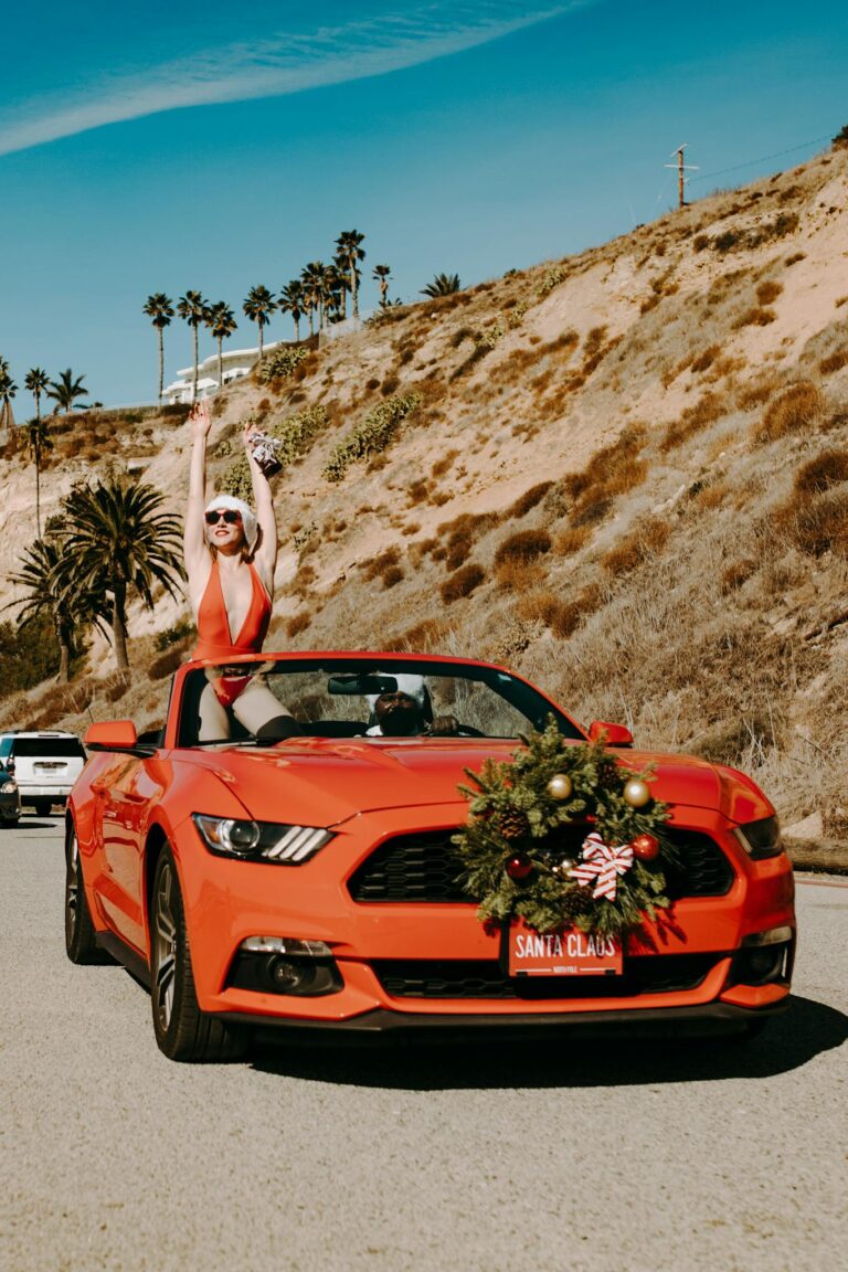 A festive red convertible car with Christmas decor on a scenic coastal drive.