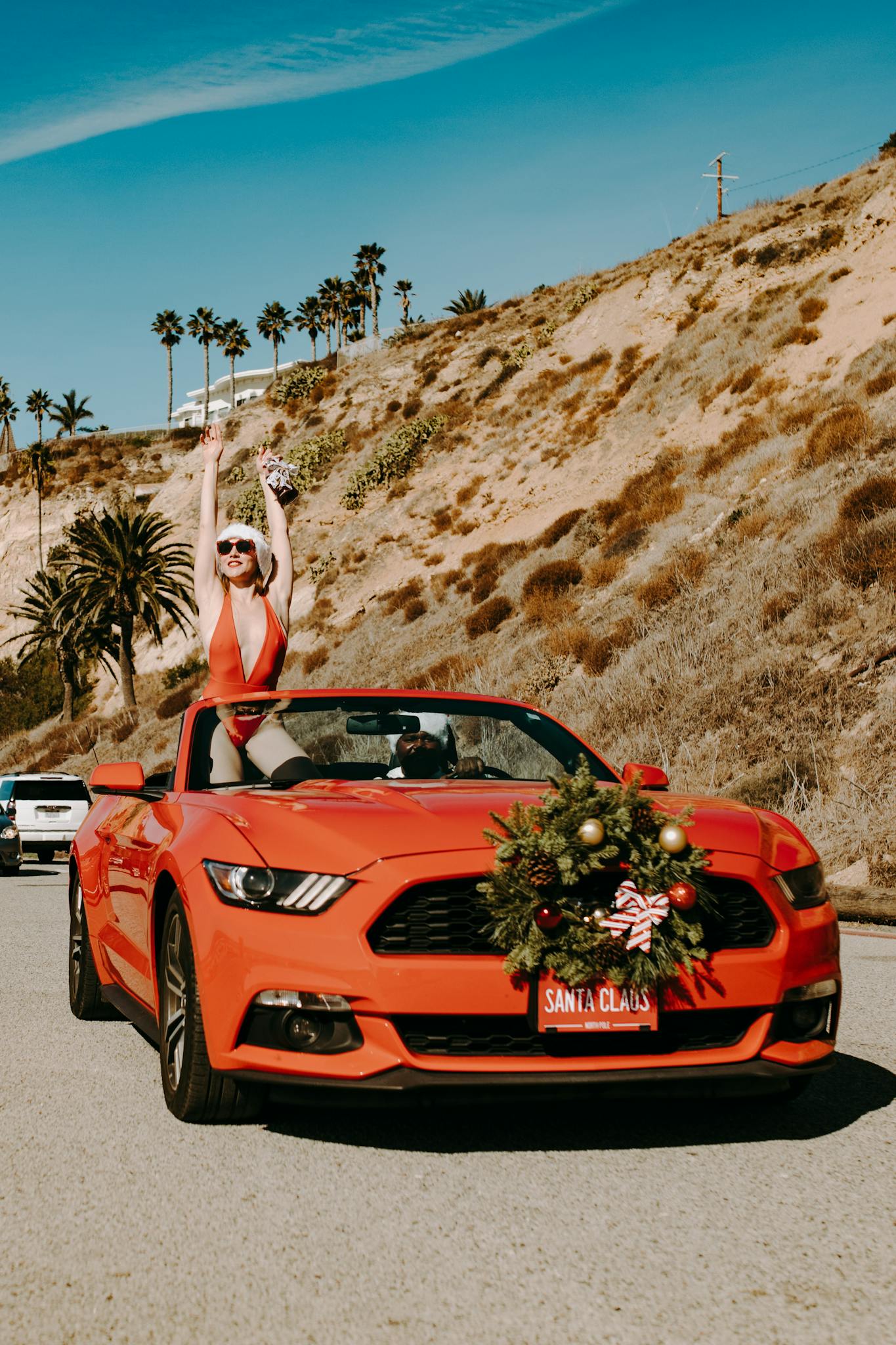 A festive red convertible car with Christmas decor on a scenic coastal drive.