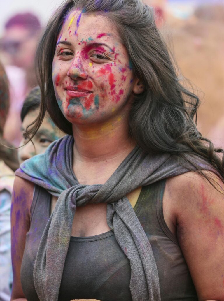 A woman joyfully participates in a Holi festival, covered in bright colorful powders.